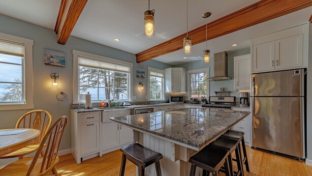 A modern kitchen with a large island, wooden ceiling beams, and pendant lighting.