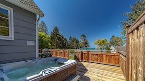 A wooden deck with a hot tub and seating area, overlooking a body of water and trees.