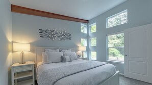 Un dormitorio con una cama grande, dos mesitas de noche, un cuadro en la pared y varias ventanas.