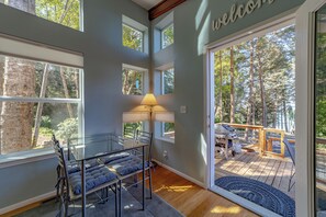 A room with a glass table, chairs, and a lamp. There is a deck with a barbecue grill and a welcome sign. - Comfy oceanside retreat, forested creekside setting, expansive grounds over ocean bluffs (Trinidad)