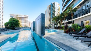 Une piscine dotée de chaises longues et offrant une vue dégagée sur les grands immeubles qui se dressent à l’arrière-plan.