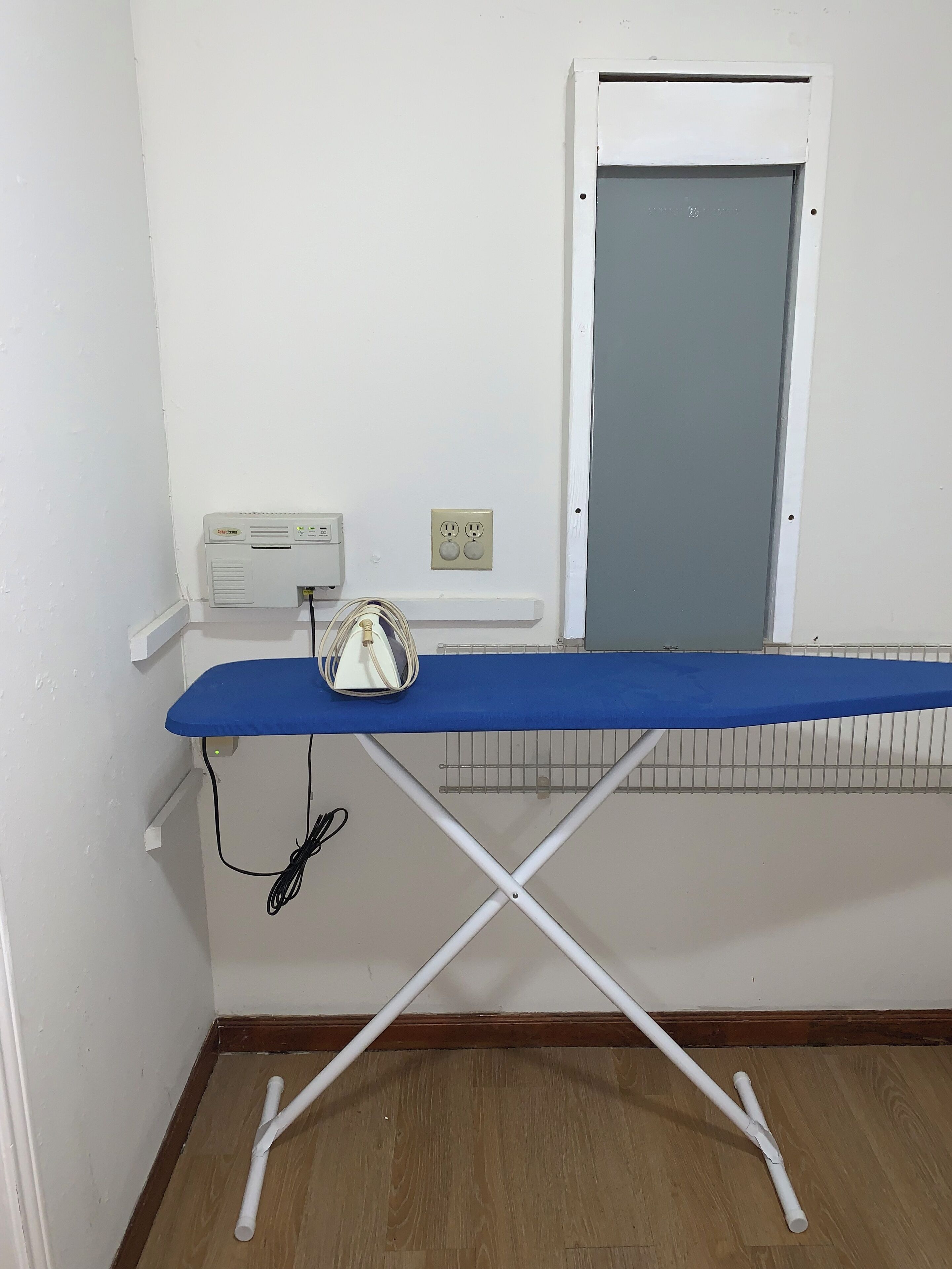 Une pièce avec une planche à repasser bleue, une prise de courant et une fenêtre avec une porte fermée.