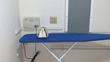 Une pièce avec une planche à repasser bleue, une prise de courant et une fenêtre avec une porte fermée.