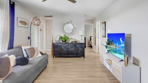 A modern living room with a grey sofa, a dark wooden cabinet, and a flat-screen TV on a white stand. - Cozy Florida Retreat (Dade City)