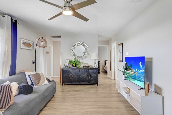 A modern living room with a grey sofa, a dark wooden cabinet, and a flat-screen TV on a white stand. - Cozy Florida Retreat (Dade City)