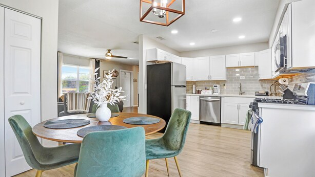 A modern kitchen with white cabinets, a black refrigerator, and a dining area with teal chairs and a wooden table. - Cozy Florida Retreat (Dade City)
