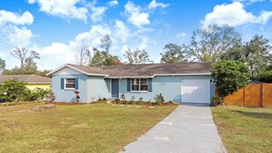 A single-story house with a front garage, a concrete driveway, and a well-maintained lawn. - Cozy Florida Retreat (Dade City)