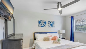 A bedroom with a bed, a ceiling fan, a TV mounted on the wall, and two wall art pieces. - Cozy Florida Retreat (Dade City)