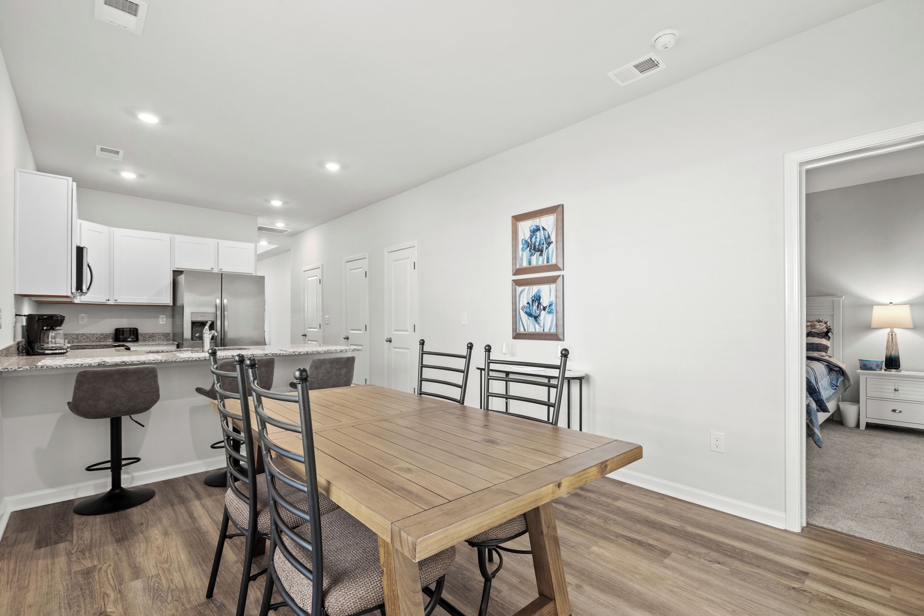 Una cocina moderna con armarios blancos, una mesa de comedor de madera y taburetes de bar. Hay dos cuadros en la pared.