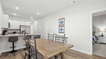 Una cocina moderna con armarios blancos, una mesa de comedor de madera y taburetes de bar. Hay dos cuadros en la pared.