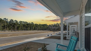 A porch with teal chairs, a view of a road, and a forest in the background. - 3-bedroom townhome in amazing Calabash next to Meadowlands Golf Course & Beach (Calabash)