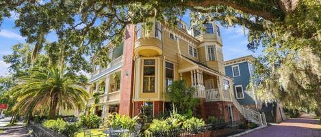 A historic building with a prominent bay window, a brick facade, and a large porch area.