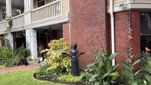 Ein Gebäude mit einer Veranda, einer Statue und einem Garten mit verschiedenen Pflanzen.