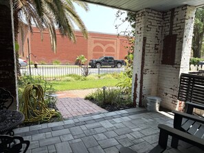 A covered patio area with a brick wall, a bench, and a hose coiled on the ground. - Private studio/parking in historic mansion, close to forsyth park, dogs welcome (Savannah)