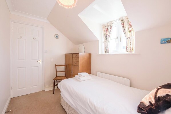 A bedroom with a bed, a wardrobe, a chair, a window with floral curtains, and a door. - 3 Barley Lands, Aldeburgh (Aldeburgh)