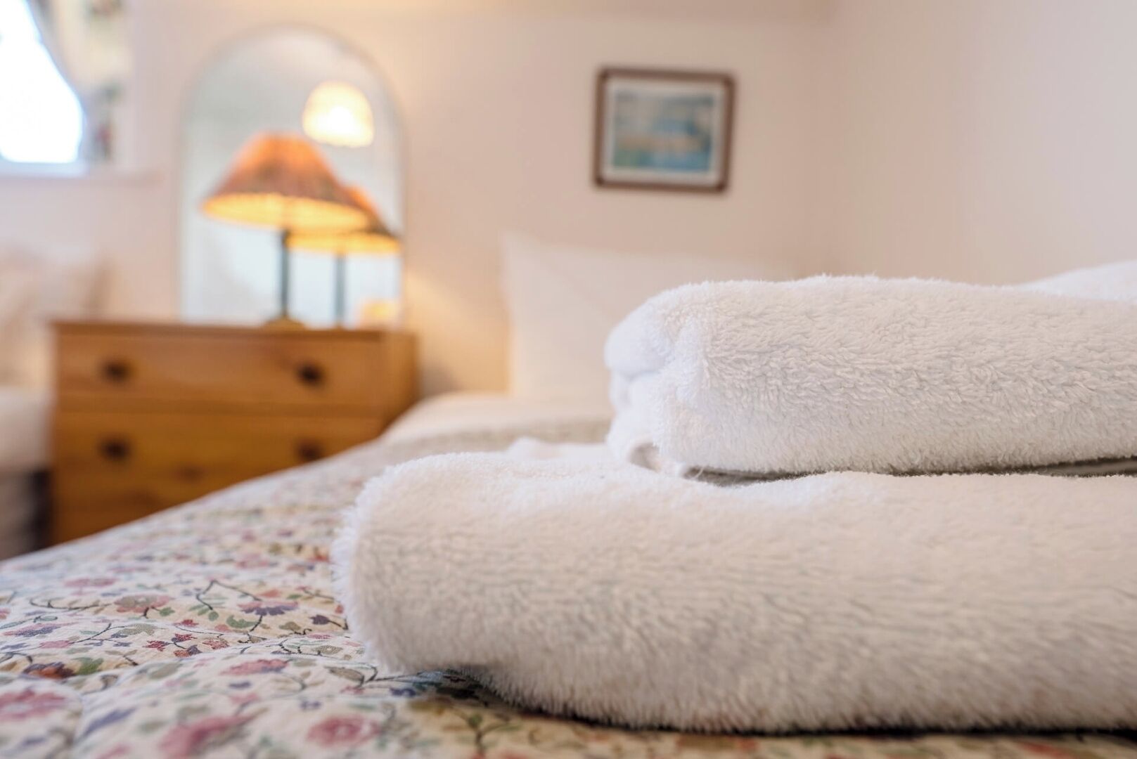 Una cama bien hecha con una colcha estampada con motivos florales y dos toallas blancas dobladas.