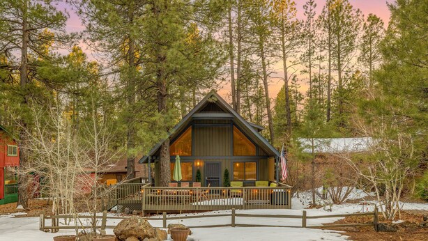 A lodge with a wooden exterior, a porch with chairs, and a view of tall pine trees.