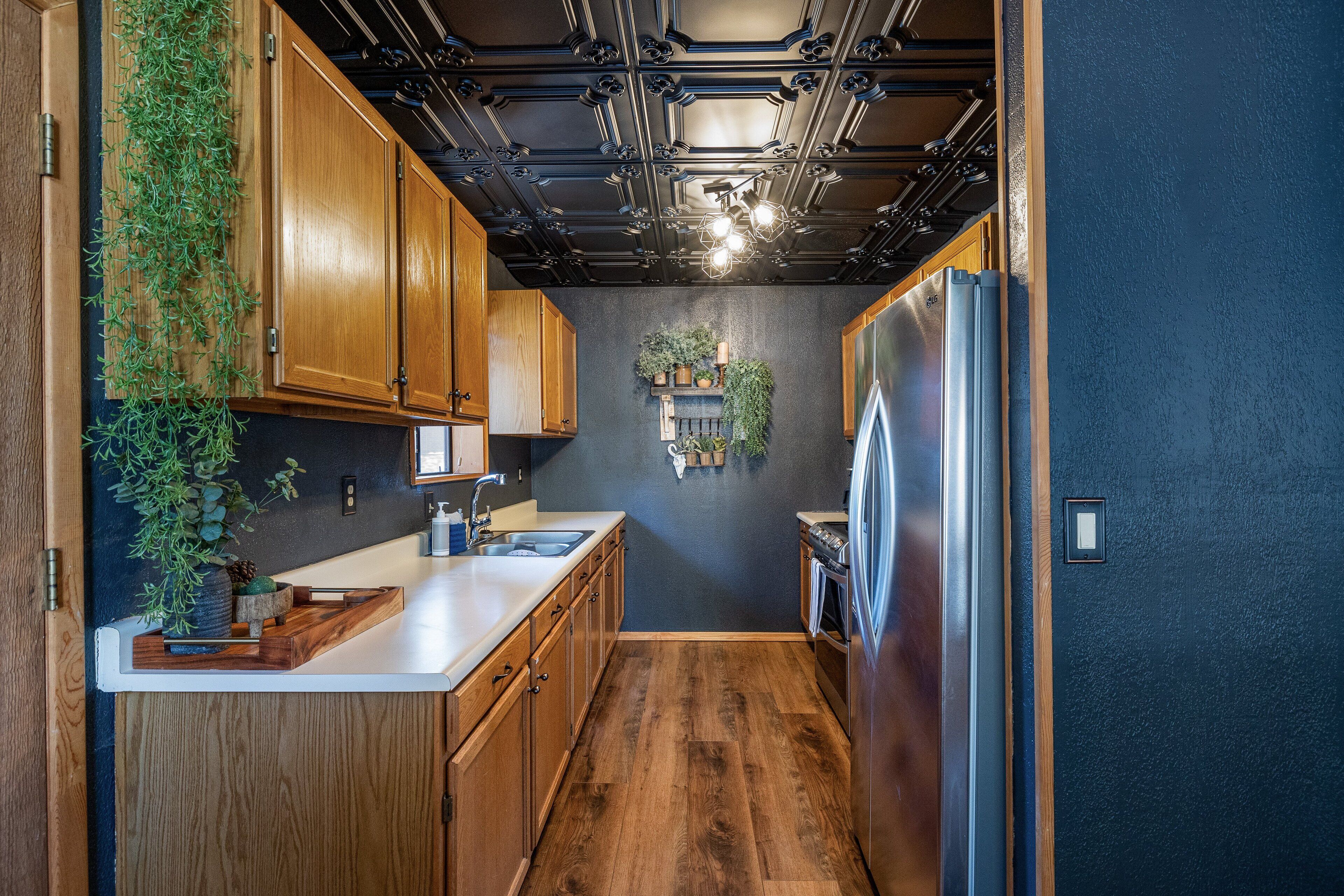 A kitchen with wooden cabinets, a stainless steel refrigerator, and a black ceiling with exposed pipes.