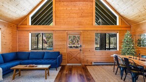 A log cabin interior with a wooden ceiling, a blue sofa, a dining table with chairs, and a Christmas tree.