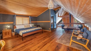 A cozy bedroom with a wooden ceiling, a bed, a nightstand, and a window with blinds.