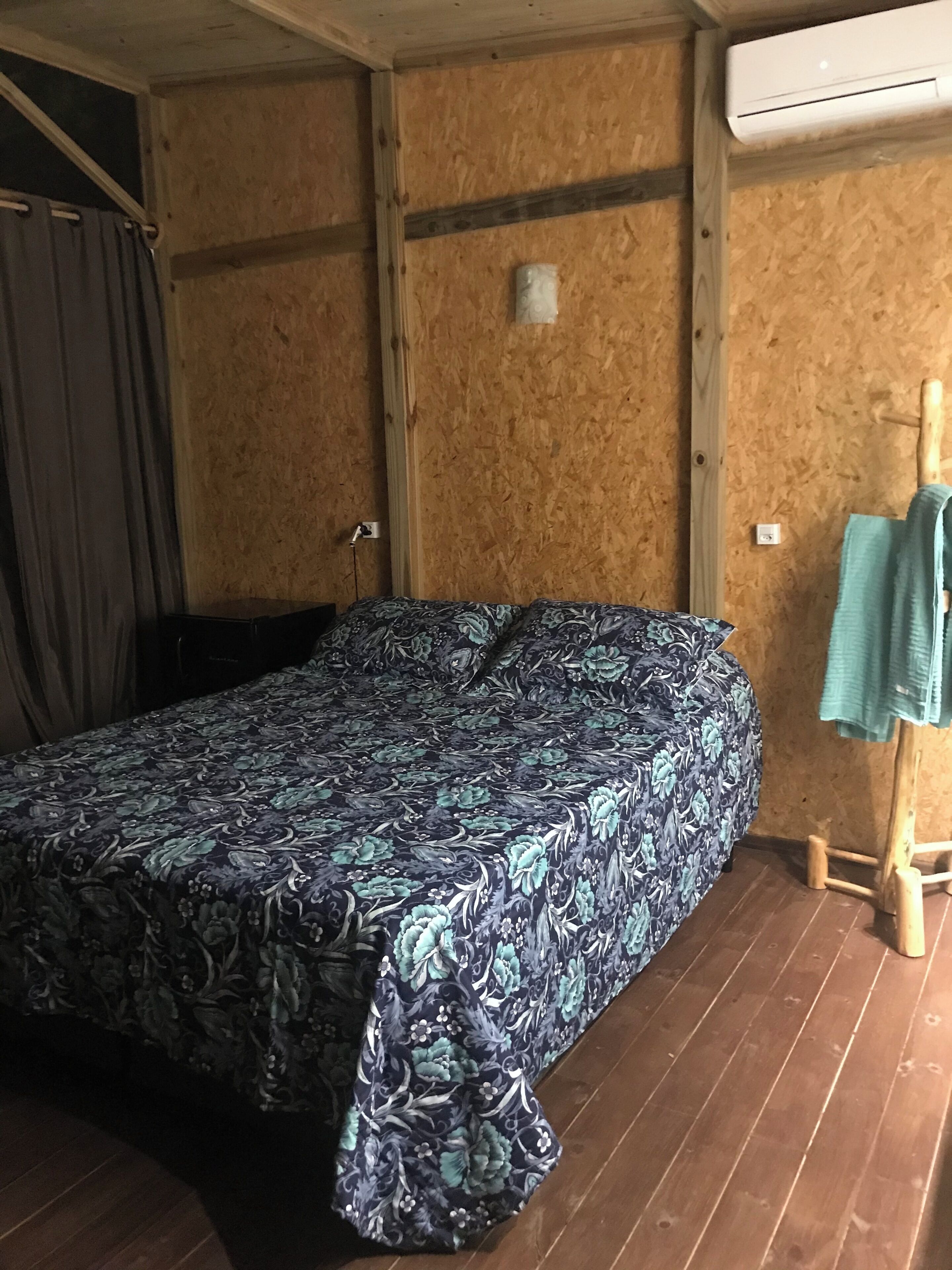 Una stanza con un letto, pareti in legno, un condizionatore d'aria e un pavimento di legno.