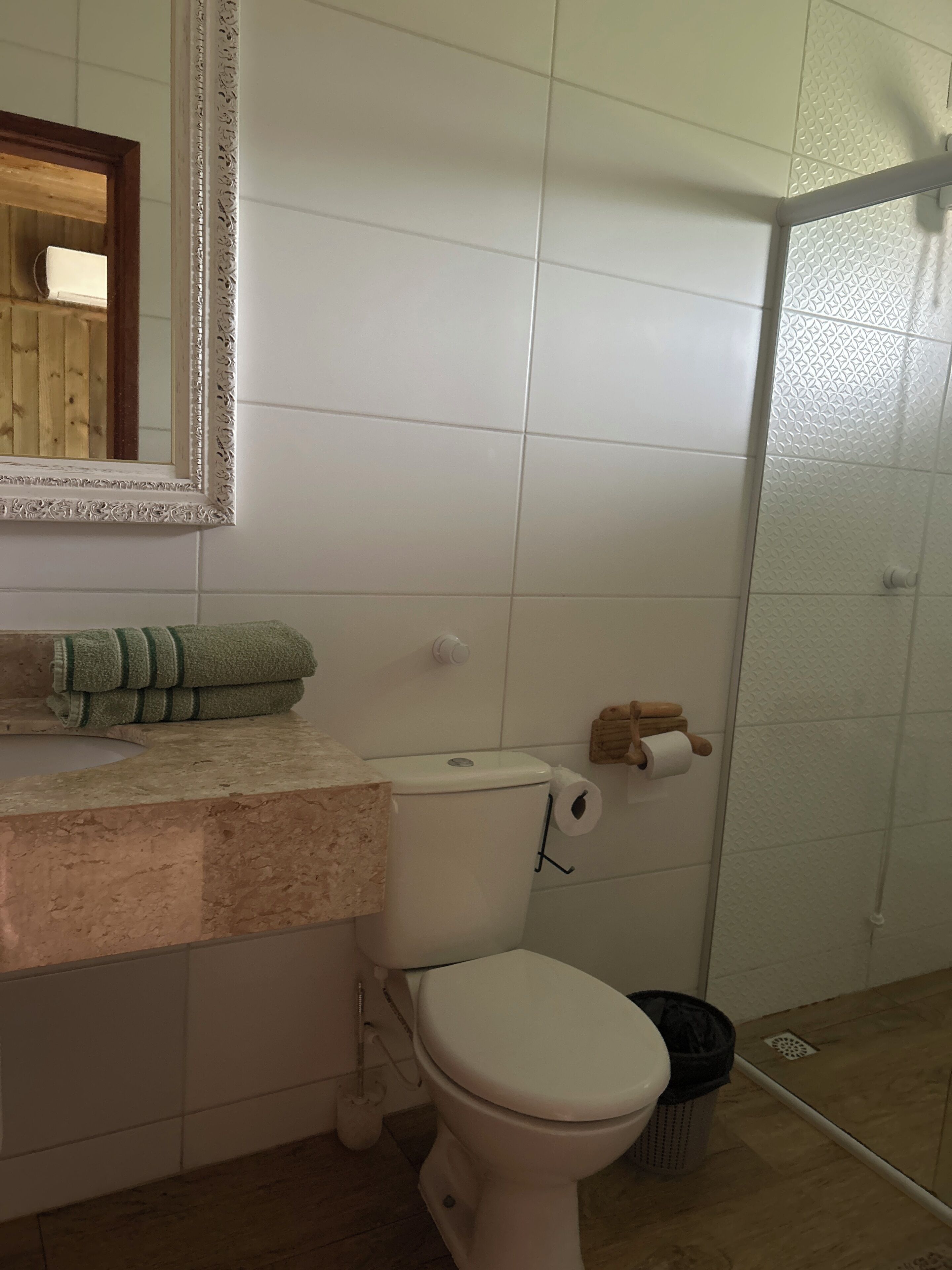 Un baño con inodoro, lavamanos con toalla, espejo y zona de ducha.