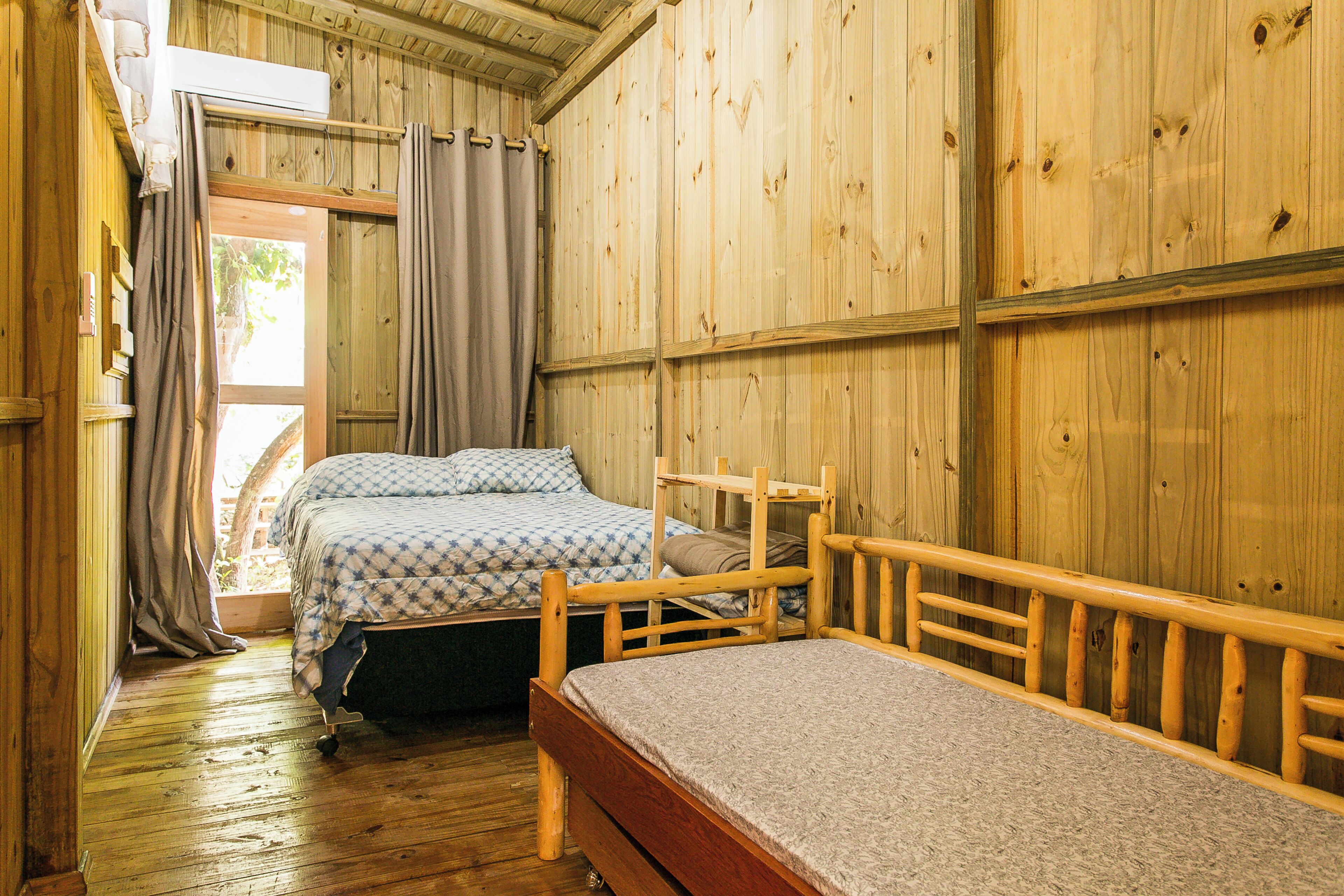 Una habitació de fusta amb dos llits, una finestra amb cortines i un terra de fusta.