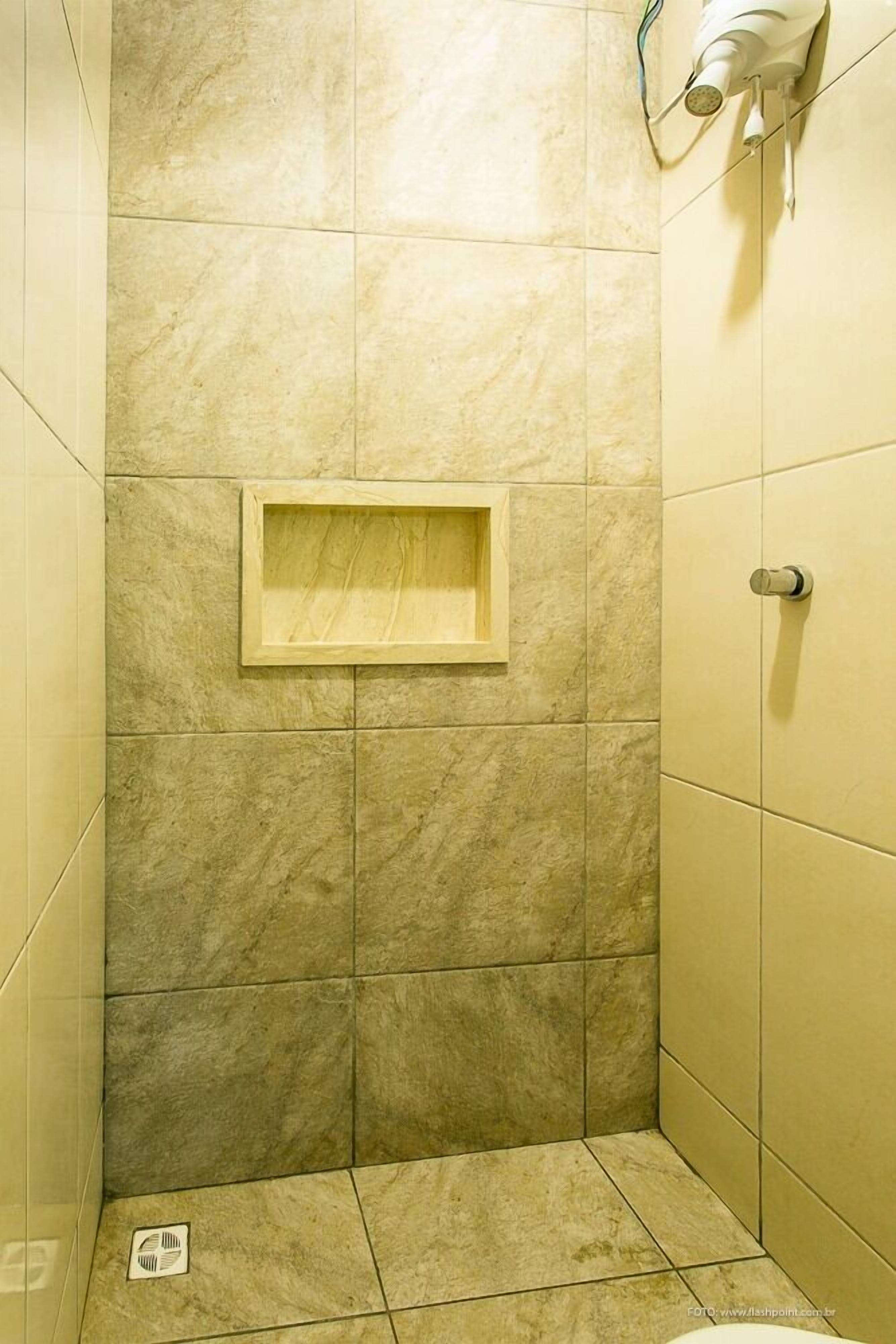 Un espacio de ducha pequeño con azulejos, un estante de madera y un perchero.
