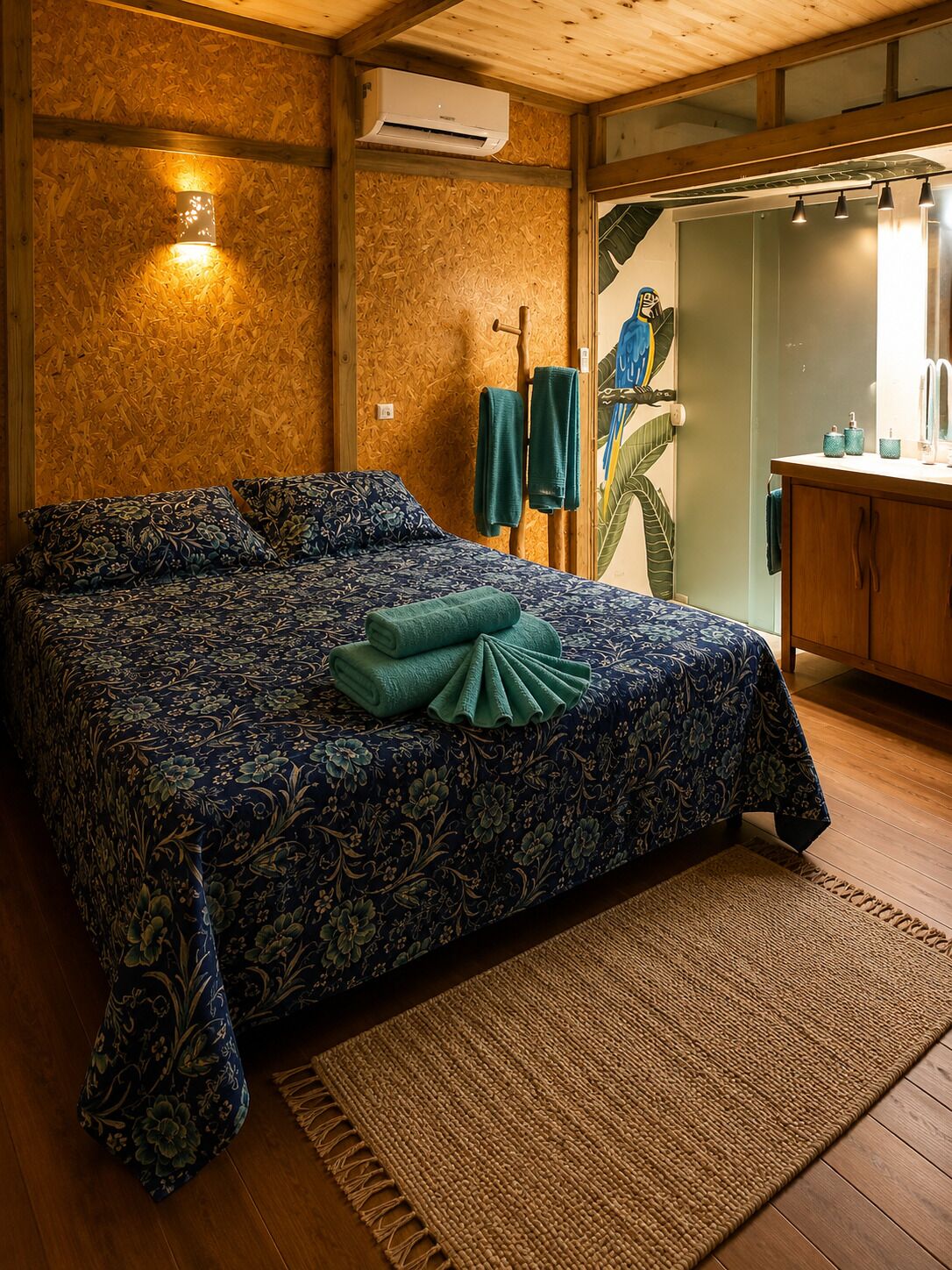 Un dormitorio con una cama grande, piso de madera, aire acondicionado de pared y un baño visible a través de una puerta abierta.