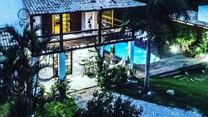 A two-story house with a swimming pool, surrounded by greenery and hills. - Pousada guarda beach house (Palhoca)