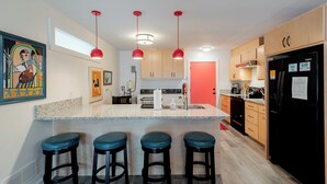 Una cocina moderna con una isla central, taburetes de bar, armarios de madera y un refrigerador negro.