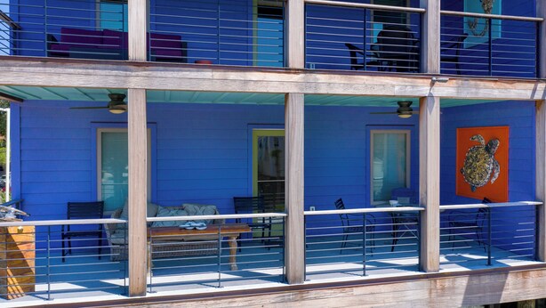 Un edificio de varios pisos con balcón, mobiliario exterior y un gran ventanal.