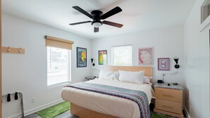 Un dormitorio con cama, mesita de noche, ventilador de techo y ventana con persianas.
