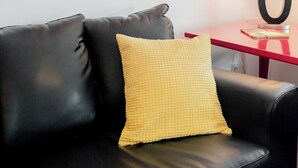 Un sofá de cuero negro con un cojín amarillo, una obra de arte abstracta enmarcada en la pared y una mesita de noche roja con una lámpara.