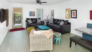 Un salón moderno con un sofá de cuero negro, un sillón de mimbre, una mesa de centro verde azulado y un reposapiés azul.