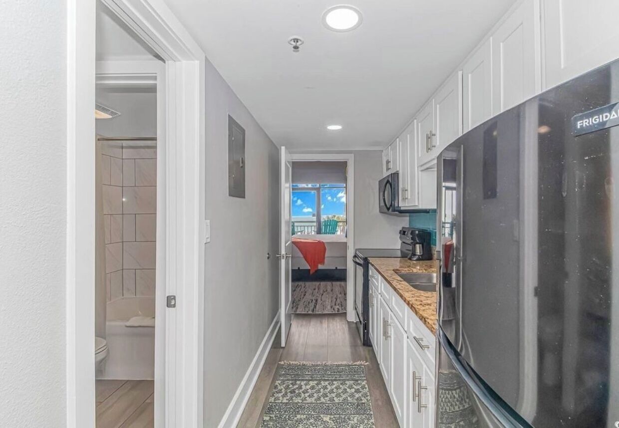 A narrow hallway leading to a bathroom and a kitchen area with a refrigerator and microwave.