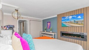 Una habitación de hotel moderna con cama, televisor montado en la pared, una mesita con dos plantas en macetas y una chimenea.