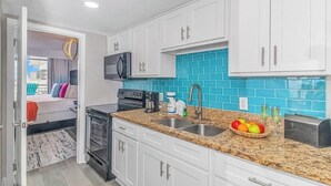 Una cocina compacta con armarios blancos, microondas, cafetera y tostadora.