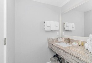 A bathroom with a marble sink, white towels, and a hairdryer on a stand. - Beach'n 1BR Ocean Front Condo Arcades Fireplace (Myrtle Beach)