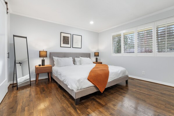 A bedroom with a bed, two bedside tables, a mirror, and a window with blinds.