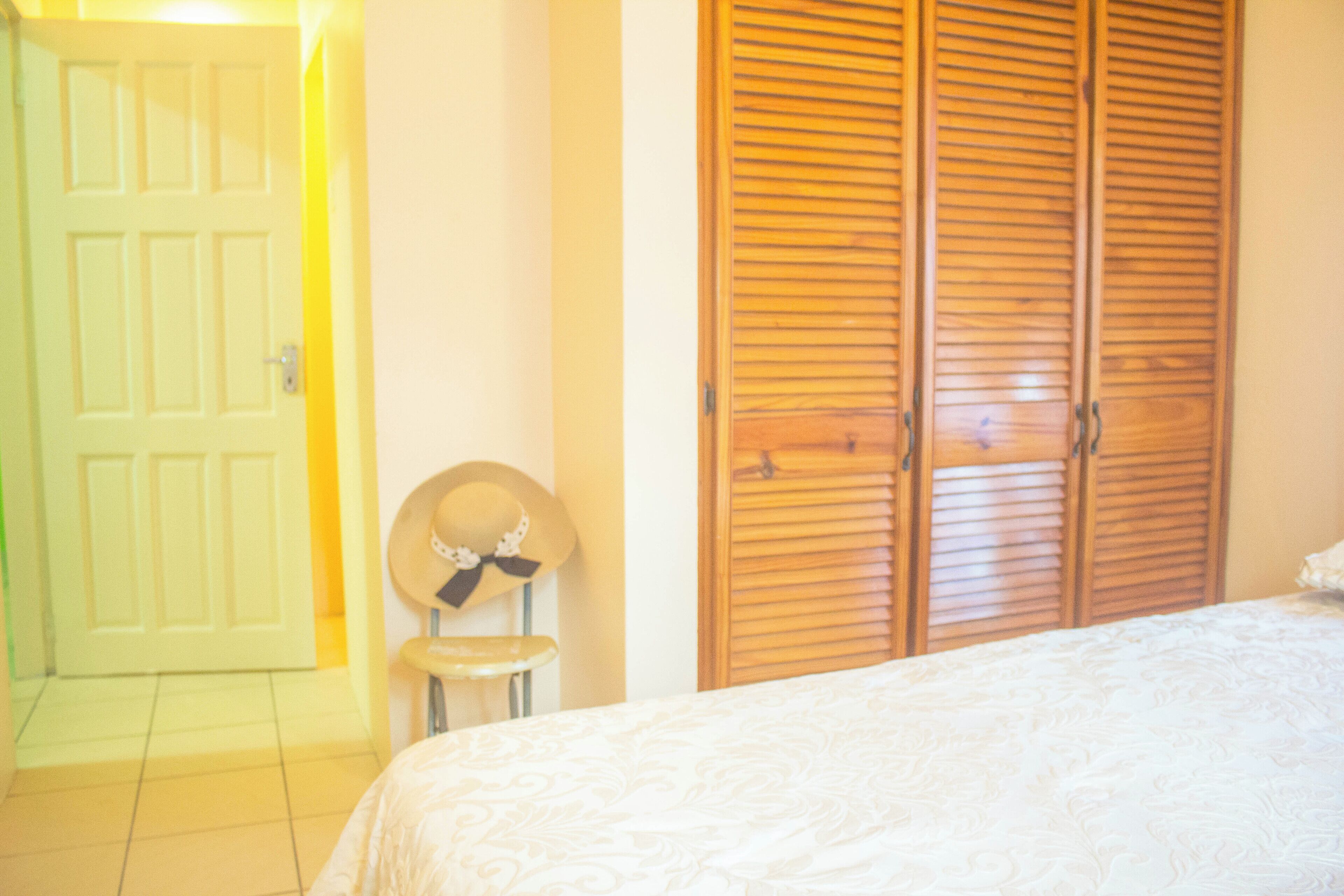 A bedroom with a bed, a wooden wardrobe, a door, and a hat on a stool.
