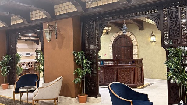 A lobby with a reception desk, two blue armchairs, and potted plants. - Wow Al Zahra Apartments (Jeddah)