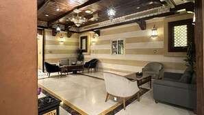 A spacious living area with a high ceiling, exposed wooden beams, and a marble floor. There are several seating options including a sofa, chairs, and a dining table. - Wow Al Zahra Apartments (Jeddah)