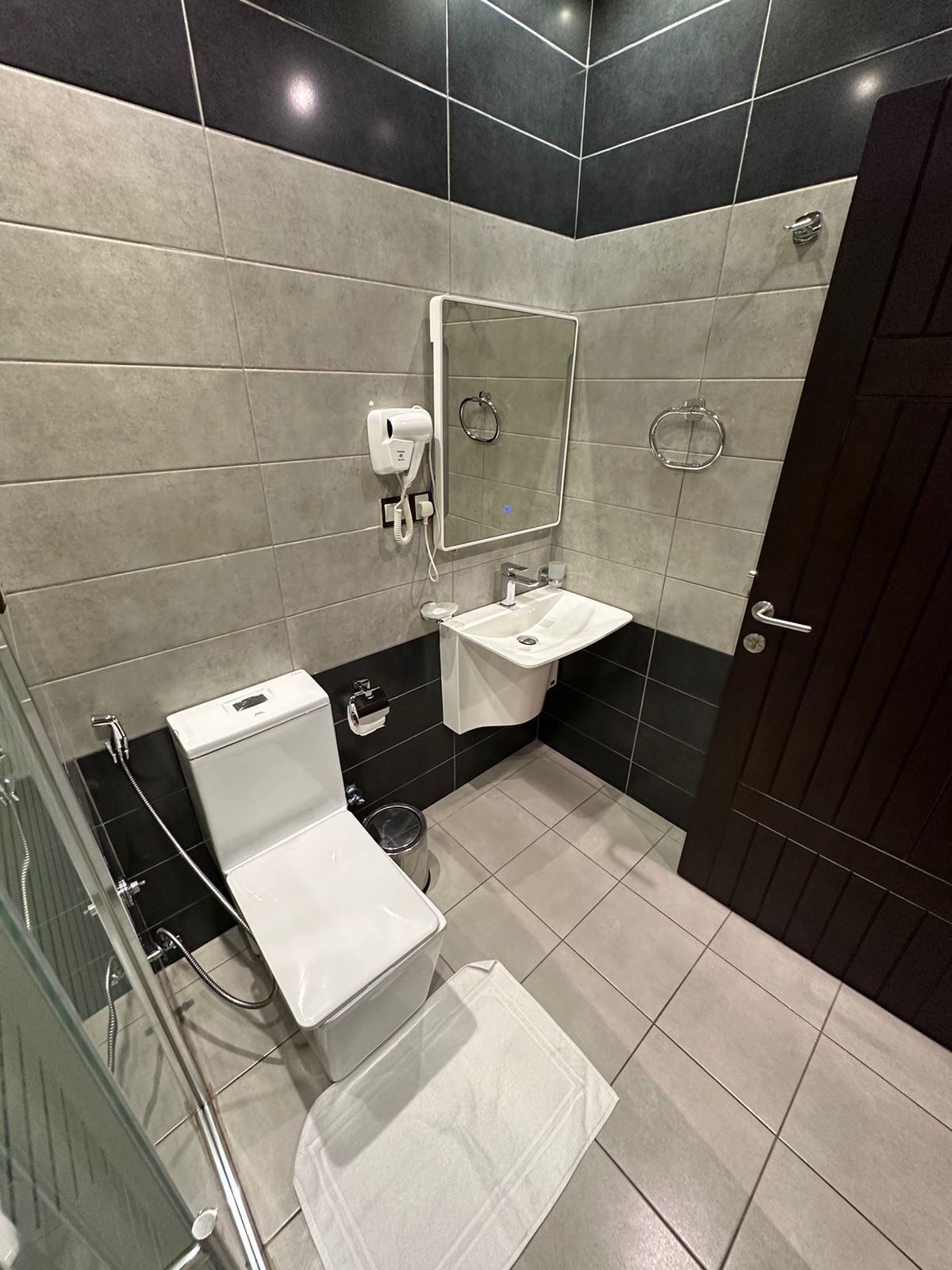 Egy modern fürőszoba, amelyben WC, mosdókagyló és zuhanyzó található.