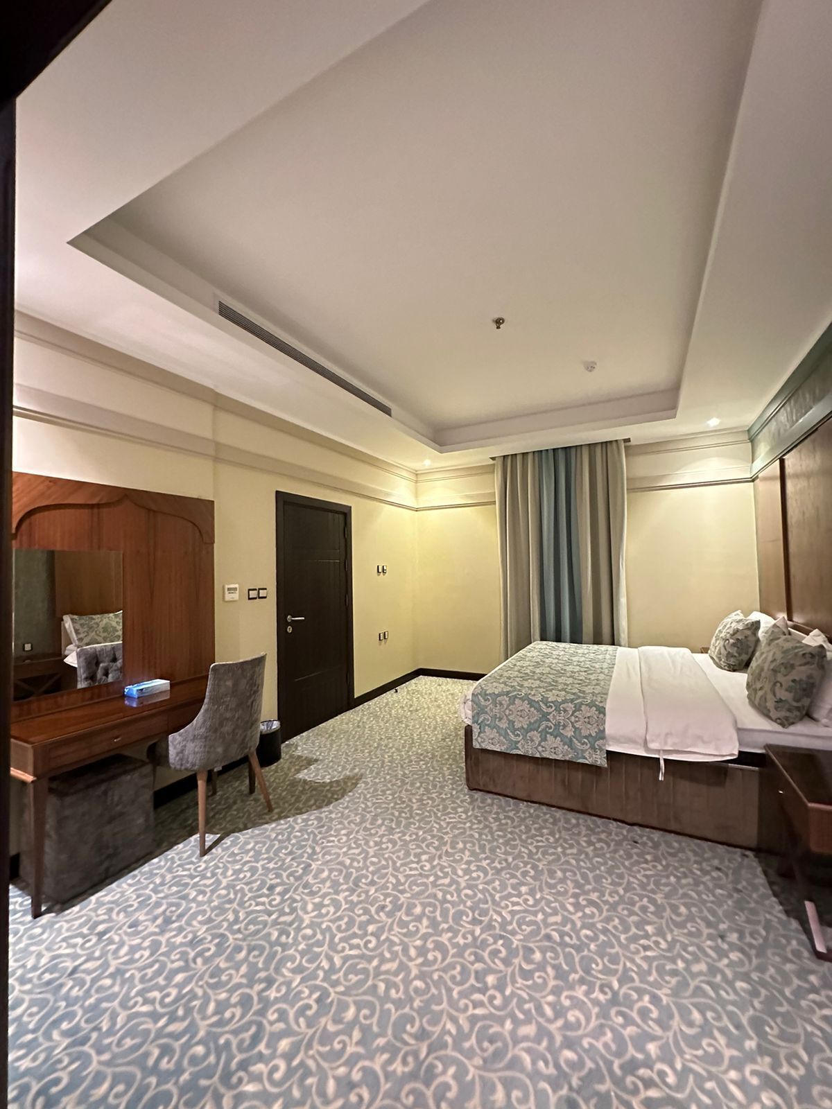 A hotel room with a bed, a desk with a chair, a wardrobe, and a bathroom door.