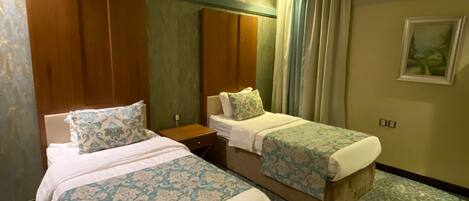 A hotel room with two beds, a wooden wardrobe, a nightstand, and a painting on the wall.