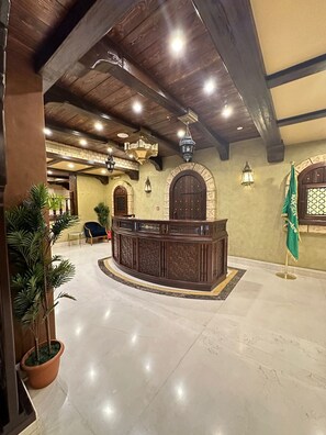 A lobby with a reception desk, potted plants, and a flag. - Wow Al Zahra Apartments (Jeddah)