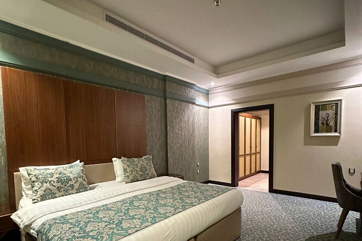 Ein Hotelzimmer mit einem großen Bett, einem hölzernen Kopfteil, einem Schreibtisch und einem gemusterten Teppich.