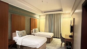 A hotel room with two beds, a desk, a chair, a TV, and a patterned carpet. - Wow Al Zahra Apartments (Jeddah)