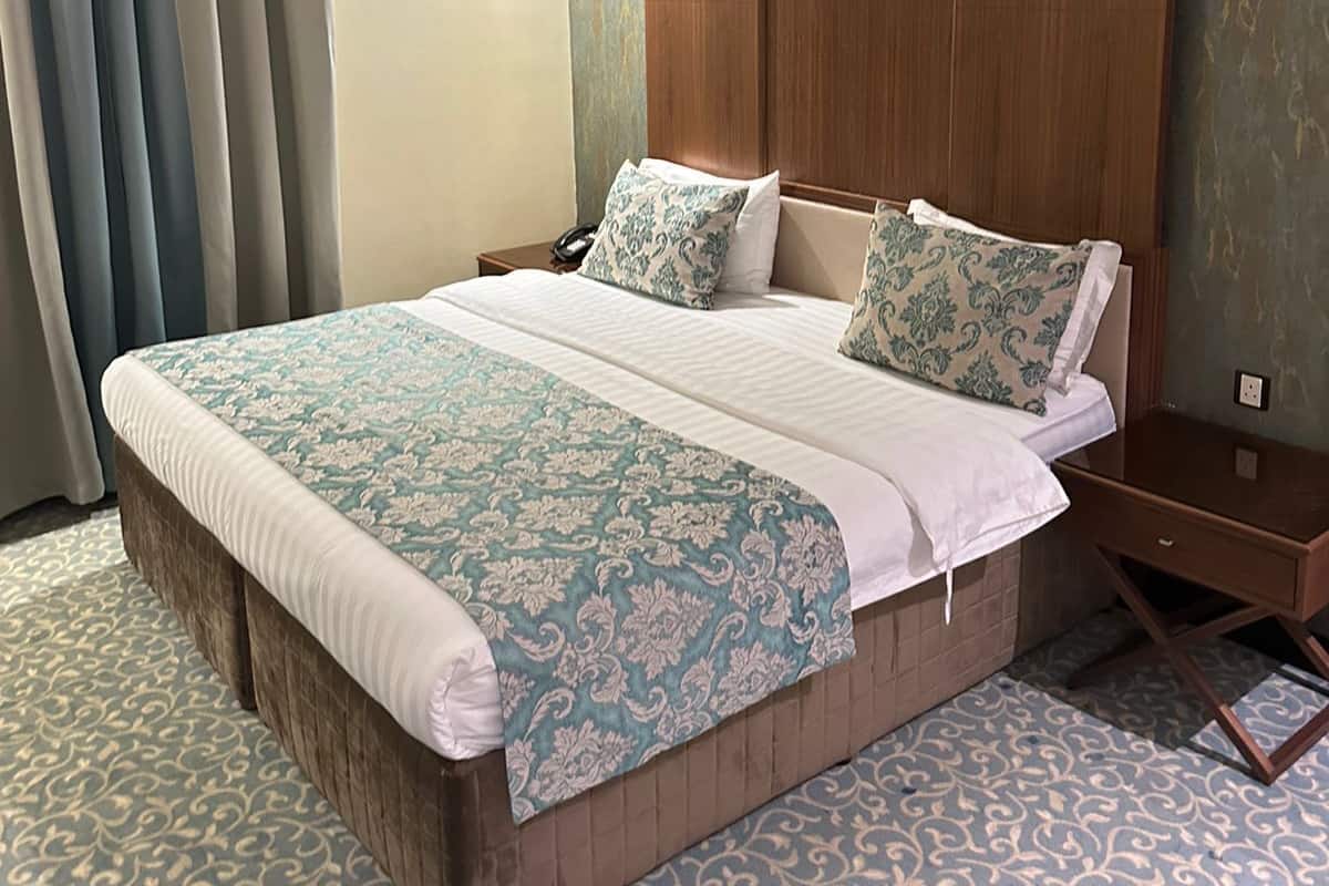 Ein Hotelzimmer mit einem großen Bett, einem Holzkopfstück, einem Nachttisch und einem gemusterten Teppich.